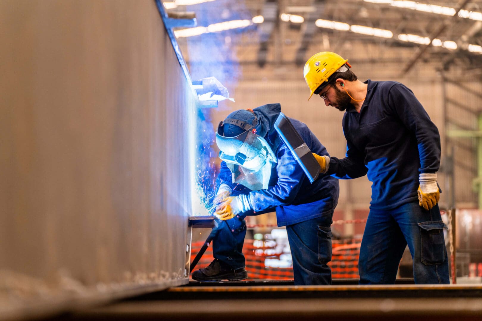 Two workers welding metal in an industrial setting.