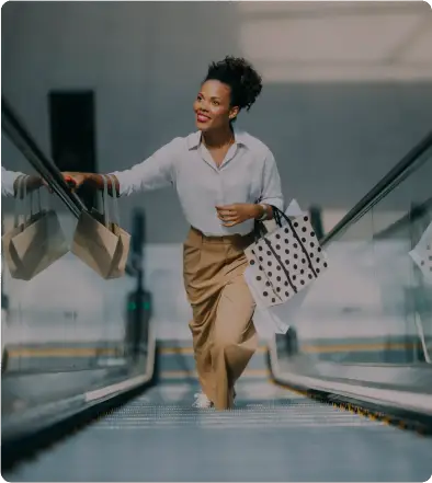 A joyful woman ascending an escalator with shopping bags and a bowl.