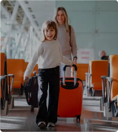 A child pulls a suitcase with an adult following in an airport terminal.