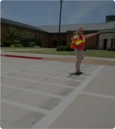 A person standing in a parking lot near a building on a sunny day.