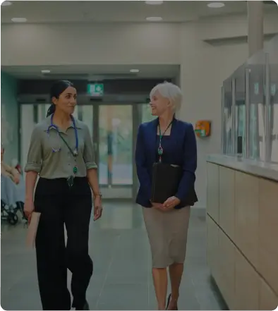 Two professional women walking and talking in a modern office hallway.