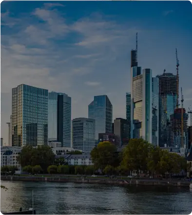 Modern city skyline with tall skyscrapers by a river under a cloudy sky.