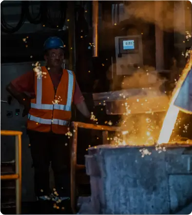 Worker in safety gear pouring molten metal in a foundry.