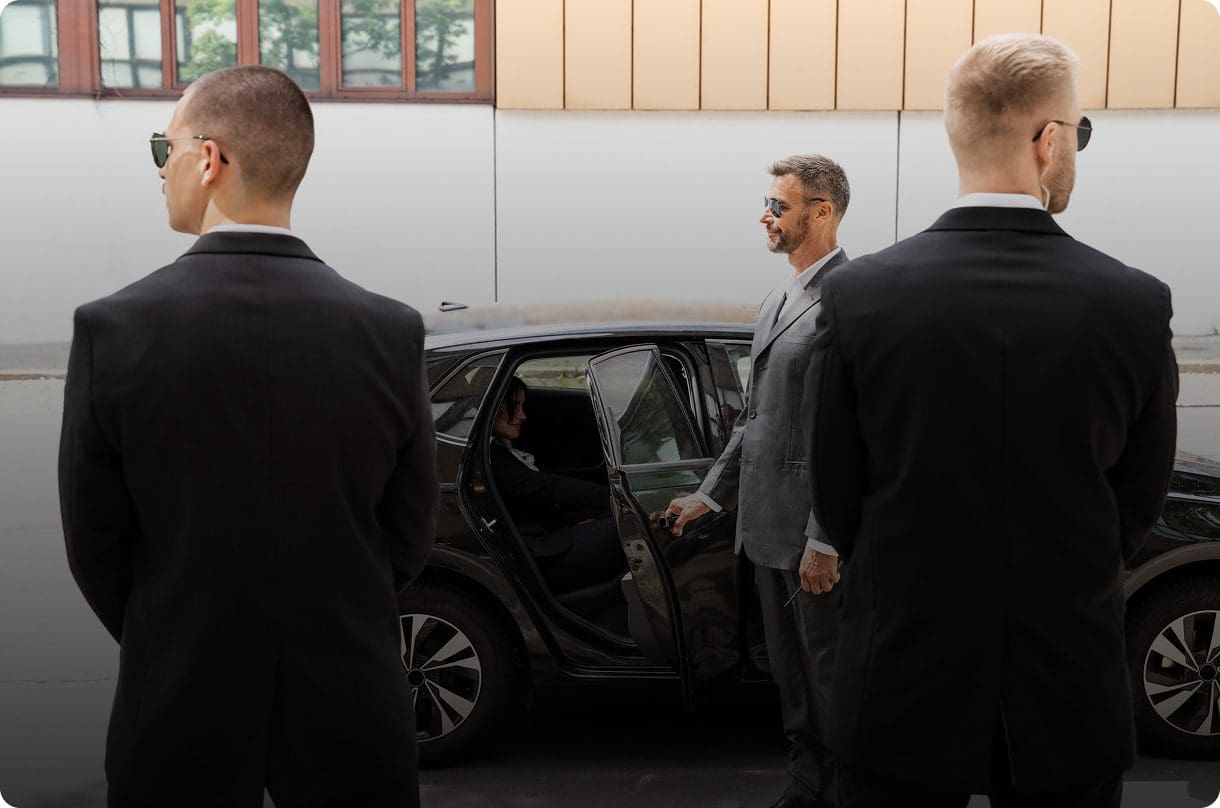 Men in suits standing near a car.